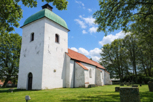 White medieval church from 1115, in green, in full sun.