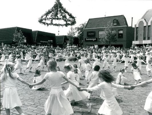 Kinderen gekleed als Pinksterbruidjes dansen rond een met bloemen versierde constructie tijdens een traditionele viering in Borne uit de vorige eeuw.