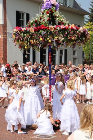 Kinderen gekleed als Pinksterbruidjes dansen rond een met bloemen versierde constructie tijdens een traditionele viering in Borne.