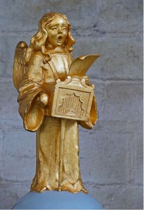 Verguld beeldje van de engel Ariëtta, staand met een klein draagbaar portatief orgel voor zich, als voorstelling van muziek en engelenzang.