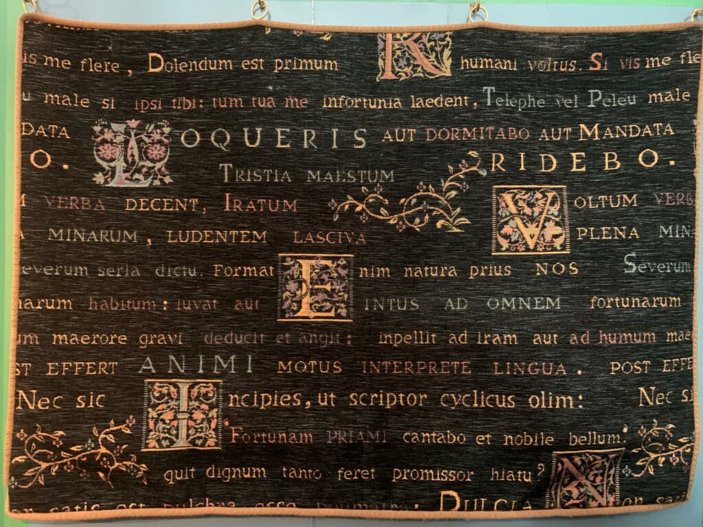 Klavierdoek van het Hillenorgel “Rechthoekig zwart beschermdoek met goud- en koperkleurige Latijnse letters, sierlijke initialen en kleine bloemmotieven. Het doek wordt over de klavieren van het orgel gelegd wanneer het niet wordt bespeeld, als bescherming tegen stof. De tekst bestaat uit passages van de Romeinse dichter Horatius over gevoel, voordracht en de kracht waarmee woorden en kunst op een ander kunnen overkomen.”