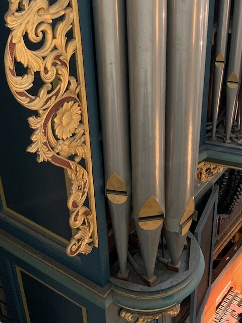 Detail van de grote orgelpijpen aan de linkerzijde van het orgel, met de hoge metalen labiaalpijpen en vergulde ornamenten van de orgelkas.
