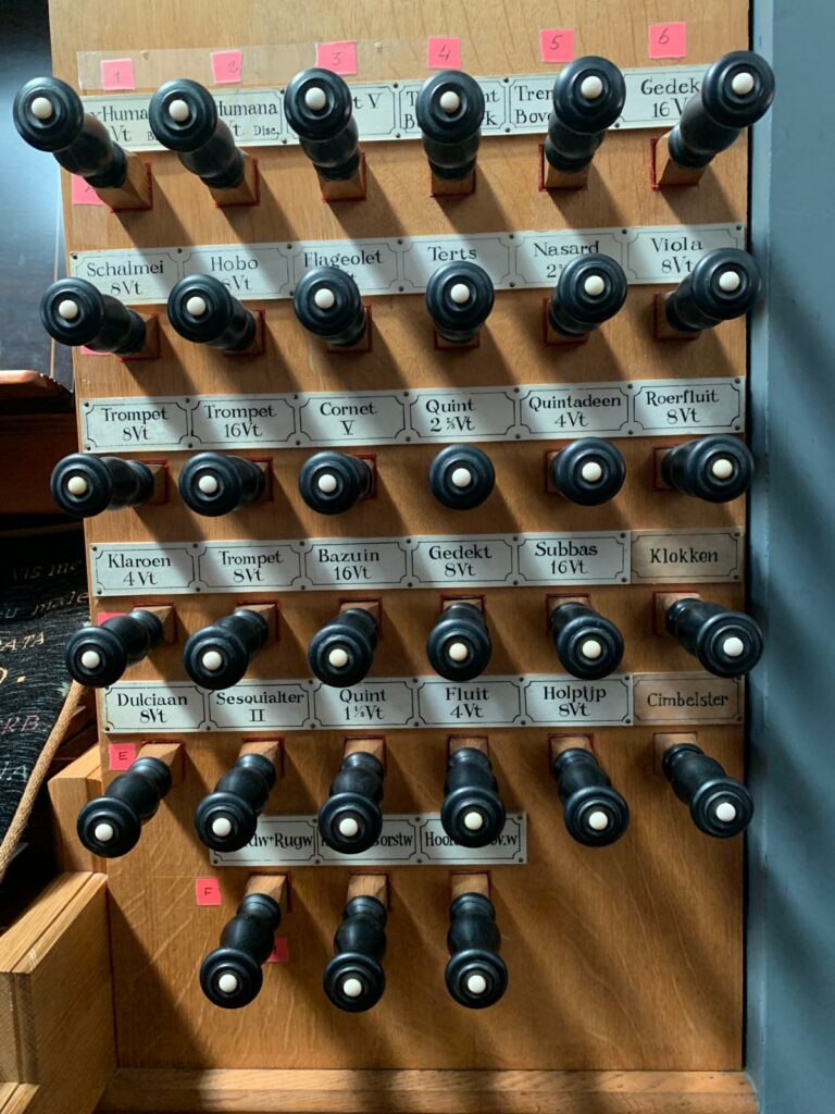 Rechter registerpaneel van de speeltafel van het Hillenorgel, met rijen zwarte registerknoppen voor onder andere trompet, hobo, cornet, viola, bazuin en andere klankkleuren.