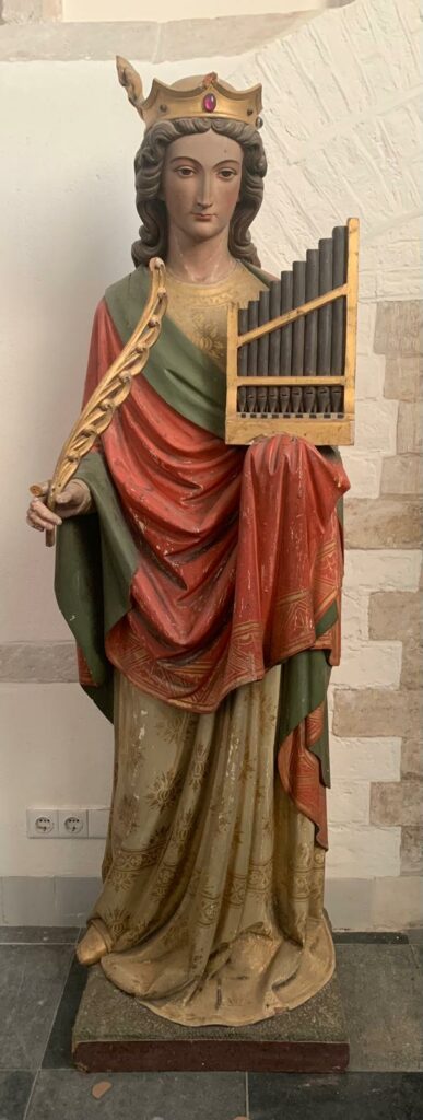 Mensgrote Beeld van Sint Cecilia uit de Grote Kerk van Breda. Zij draagt een kroon en houdt een klein draagbaar orgel vast. Sint Cecilia is in de christelijke traditie de patrones van de kerkmuziek