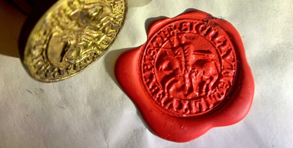 Primer plano de un sello templario en cera roja con dos caballeros sobre un mismo caballo, junto a una matriz de sello metálica.