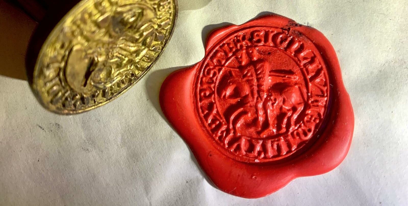 Close-up van een Tempelierszegel in rode was met twee ridders op één paard, naast een metalen zegelstempel.