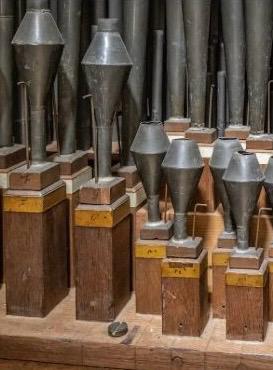 Detail van orgel-tongpijpen met hun herkenbare beker- of trechtervorm, opgesteld op houten voeten binnen in het