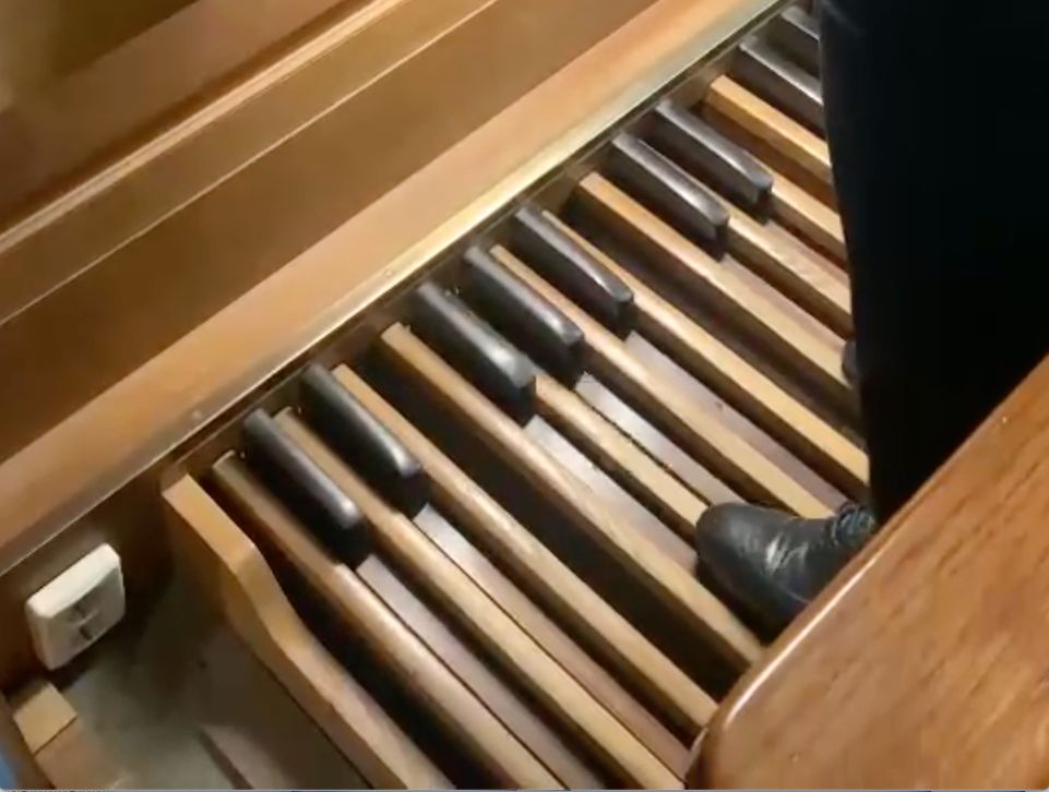 Close-up van het houten pedaalklavier van een orgel, met lange lichte en donkere pedaaltoetsen die de organist met beide voeten bespeelt.